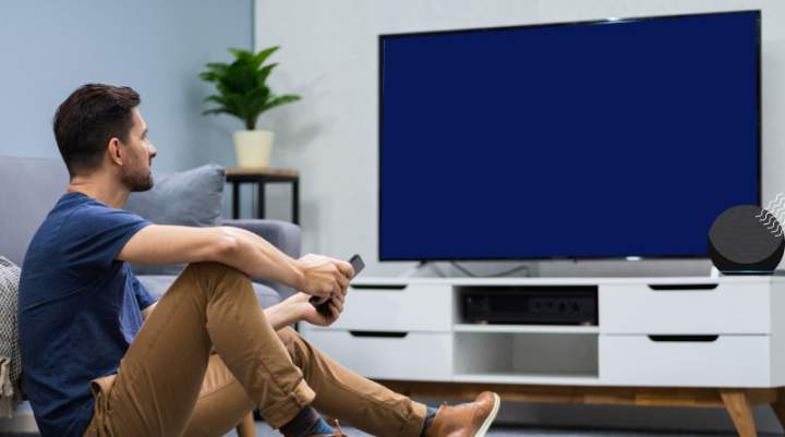 Man watching the TV which is near his smart speaker device