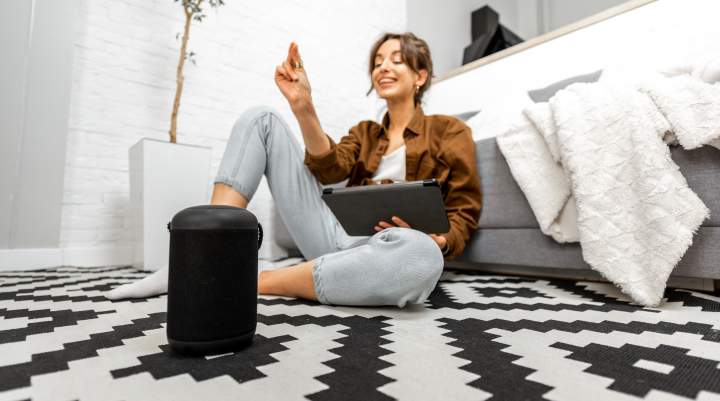 Woman sat on floor in front of sofa engaging with her smart speaker