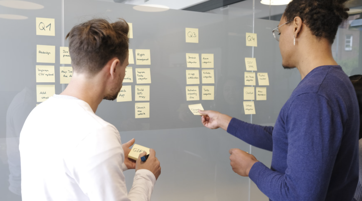 Two people looking at postit notes on a board