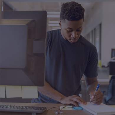 A person writing on a notepad at their desk