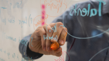 Person brainstorming onto a transparent dry-erase board