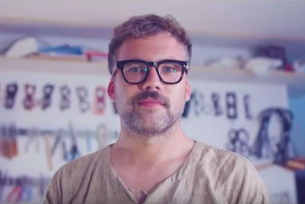 man wearing glasses standing in front of wall of glasses presenting video about his glasses company